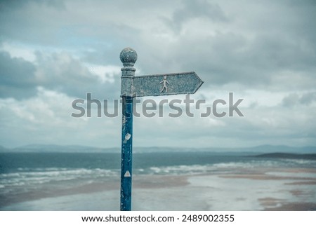 An old blue signpost in front of the beautiful cloudy, blue sea. Only a stick figure can be seen on the signpost.