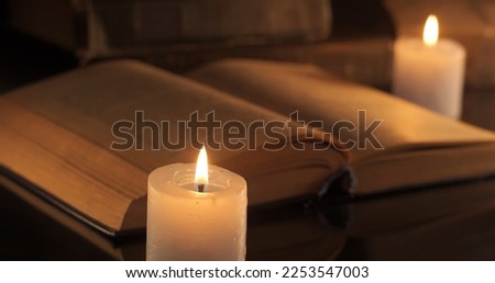An old book and burning candles. Reading and learning by candlelight at night