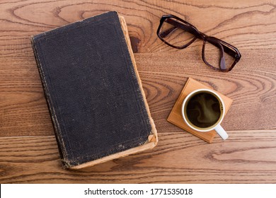 Old Book With Cup Of Coffee And Glasses. Topview Flat Lay. Brown Wooden Background.