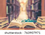 Old book in library with stethoscope on open textbook, stack piles of texts on reading desk, and aisle of bookshelves in  study class room background for medical school education learning concept