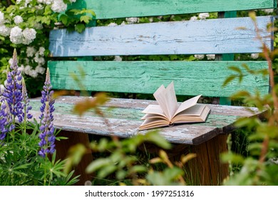 An Old Book Lies On A Dilapidated Bench In The Summer Garden. Reading As A Hobby. Camping On A Sunny Day In June. 