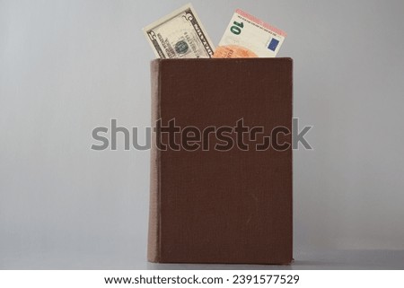 An old book with an untitled cover, showing 10 euros and five dollars, is placed on a gray background. The theme pertains to the laws of international economics and trade, the currency market 