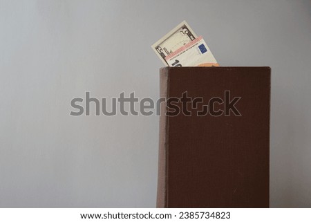 An old book with visible 10 euros and five dollars stands on a gray background. Theme of international economics and trade laws, science about economics