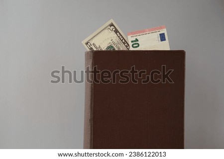 Old book with visible 10 euros and five dollars stands on a gray background. Theme of international economics 