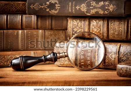 Old books and antique magnifying glass on a wooden background. An ancient book and magnifying glass as a symbol of history, education. Translation of book titles - history of England, ancient history.