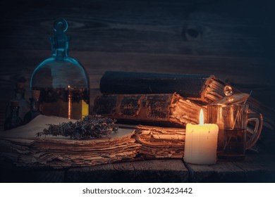 Old Books And Candle, Tincture Or Potion Bottle, Glass Of Beverage And Bunch Of Dry Healthy Herbs. 