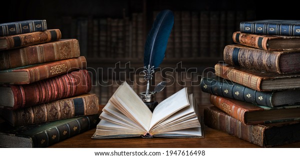 Old books ,quill pen and vintage inkwell on wooden desk in old library. Ancient books historical background. Retro style. Conceptual background on history, education, literature topics.

