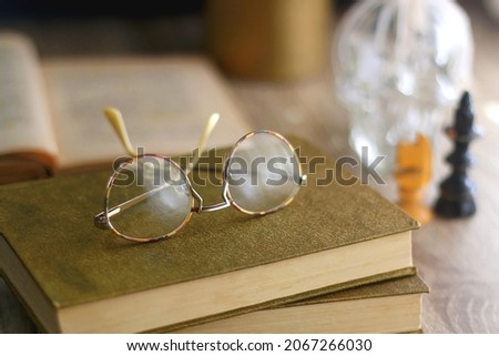 Old books, reading glasses, vintage chess pieces, lit candle and vase with gypsophila flowers. Dark academia concept. Selective focus.