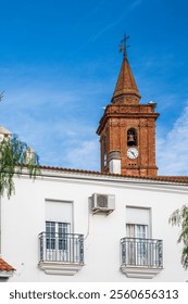 Old brick bell tower with clock and white architecture under a clear sky
