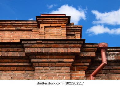 Old brick building, parapet on the roof of an  against a blurred background of blue sky with clouds.