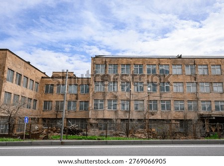 Old brick building under cloudy sky. Windows show signs of wear and neglect. Empty street suggests abandoned or underused facility. Ideal for urban decay, architectural study, or historical projects