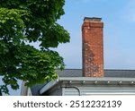 Old brick chimney with metal cap against blue sky in Brighton, Massachusetts, USA