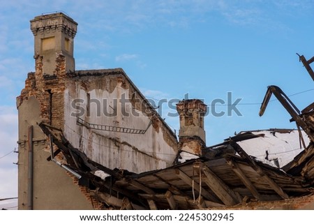 An old brick mill with a collapsed roof against the blue sky . The roof of the building collapsed due to the heavy amount of falling snow .   