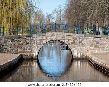 old brick stone bridge with round arch, river and trees in the background