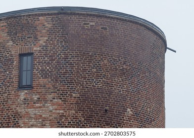 Old brick tower with a single window and gully against a cloudy sky