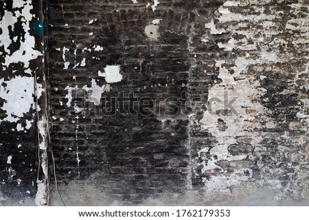 Old brick wall with black and white peeled off paint and soot and grime in a ruined factory in a lost place in Sauerland Germany. Shabby chick background with traces of former working place use.