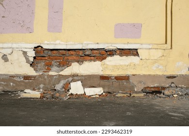 Old brick wall with plaster falling off the sidewalk