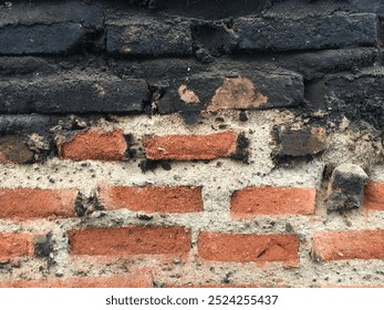 An old brick wall with a rough texture, showing signs of wear and blackened spots, likely due to exposure to fire or soot. The contrast between the red bricks and the dark patches adds character.