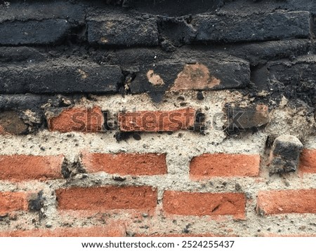 An old brick wall with a rough texture, showing signs of wear and blackened spots, likely due to exposure to fire or soot. The contrast between the red bricks and the dark patches adds character.