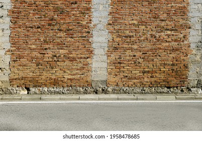 Old brick wall with three columns of exposed rough concrete blocks.Cement sidewalk and asphalt road in front. Background for copy space