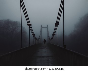 The old bridge over the river in the morning in a heavy fog and the silhouette of a man in the distance. Melancholy, depression or loneliness concept