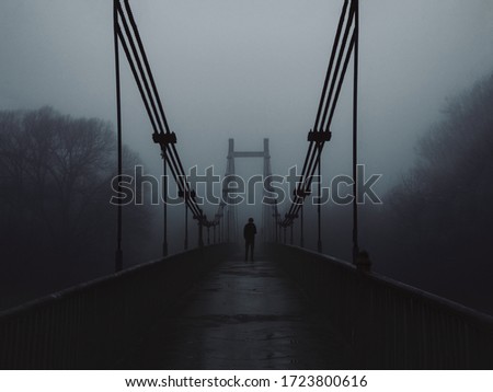 The old bridge over the river in the morning in a heavy fog and the silhouette of a man in the distance. Melancholy, depression or loneliness concept