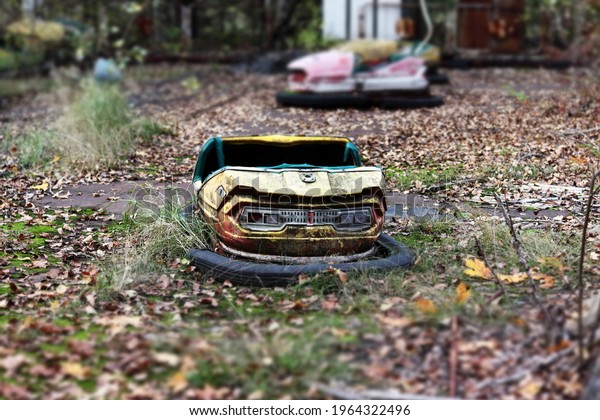 Old broken abandoned\
rusty metal radioactive yellow car among moss and autumn leaves in\
amusement park in ghost town Pripyat, Chernobyl Exclusion Zone.\
Tilt-shift effect