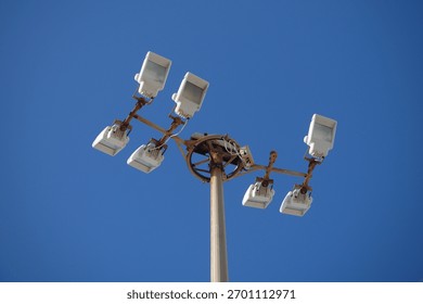 old broken array of floodlight lamps on a high post during daytime with clear blue sky 
