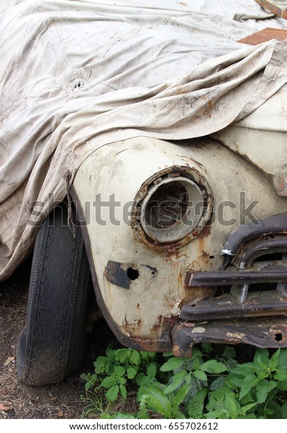 Old broken car under a\
dirty blanket