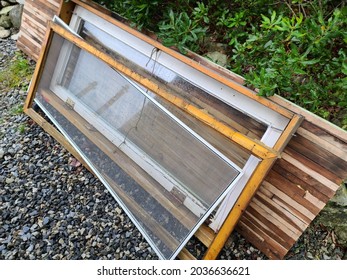 An Old Broken Door Tossed In The Vegetation. The Door Frame Is Detached From The Glass Inserts And Is Damaged Beyond Repair.