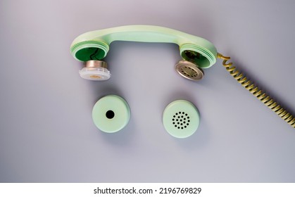 An Old Broken Green Telephone Receiver With Twisted Cord On A Gray Background. Vintage Untwisted Telephone Receiver. Disassembled Handset From A Retro Landline Phone. Top View.