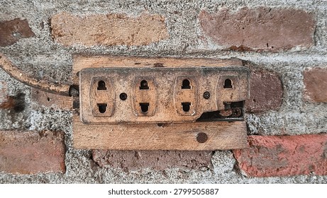 Old broken power strip socket attached to a wooden board on a rustic brick wall