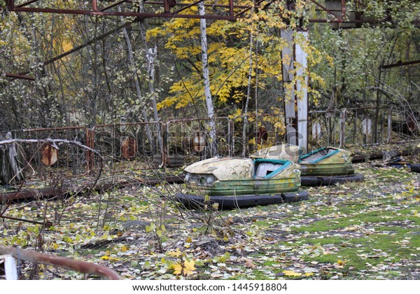 Old broken rusty metal radioactive yellow cars,\
children\'s electric cars, abandoned among vegetation, the park of\
culture and recreation in the city of Pripyat, the Chernobyl\
disaster, Ukraine.