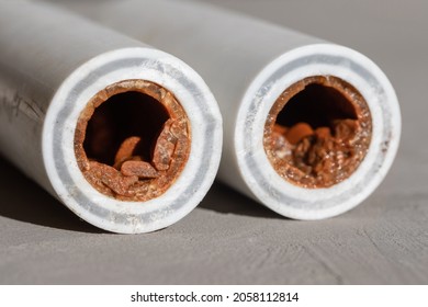Old broken sludge plumbing polypropylene pipes with red rust and limescale on concrete background with copy space. Corrosion, sludge, limescale and hard water concept