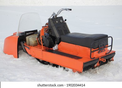 Old broken Soviet utility snowmobile without cover close up - seat, teering, engine handle and fuel tank on white snow at winter day