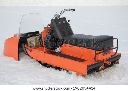 Old broken Soviet utility snowmobile without cover close up - seat, teering, engine handle and fuel tank on white snow at winter day