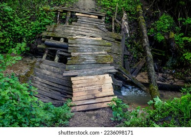 Old broken wooden bridge over a ravine with a stream
 - Shutterstock ID 2236098171