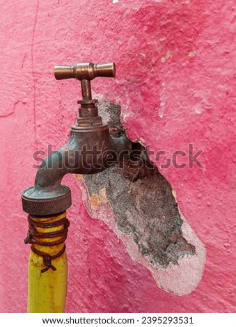 Old bronze faucet with yellow pipe and cracked cement wall.