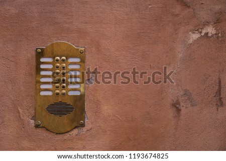 Old bronze intercom on an old wall with peeling paint. Vintage background. 