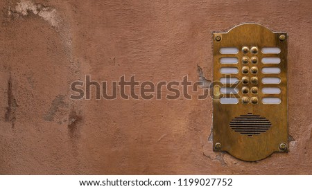 Old bronze intercom on an old wall with peeling paint. Ratio 16:9. Vintage background. 