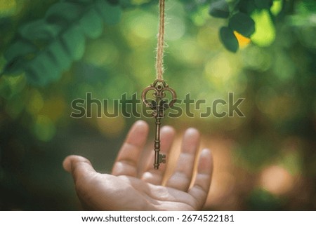 Old bronze skeleton key lying on a palm with bright sunlight and soft green bokeh, perfect symbol for unlocking doors, mystery, success, secrets and magical adventures.