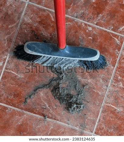 an old broom with a red handle and a pile of dust from sweeping up on a red marble tiled floor 