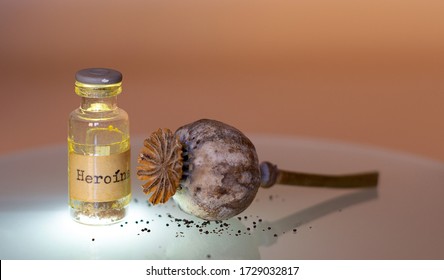 Old brown bottle of narcotic substance with HEROIN label, next to a dry opium capsule with seeds. Drugs, addictions and drug addictions