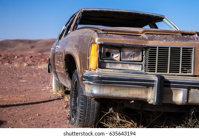 Old Brown Car With A Busted Headlight And Flat Tire In The Desert Under A Blue Sky
