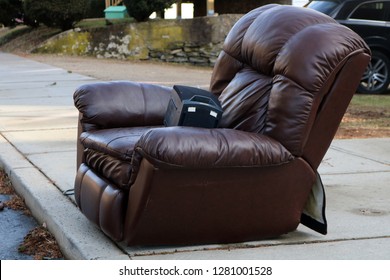 Old Brown Leather Recliner Chair Left Outside As Garbage Trash On Curb Of Urban Neighborhood