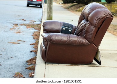 Old Brown Leather Recliner Chair Left Outside As Garbage Trash On Curb Of Urban Neighborhood