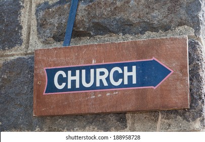 Old Brown Wood Church Sign With Blue Arrow On Dark Stone Wall