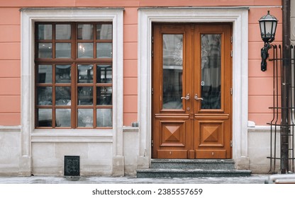 Old brown wooden window with rectangular frames for glass, a flower pot with flowers, a door and a house pink facade.