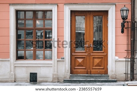 Old brown wooden window with rectangular frames for glass, a flower pot with flowers, a door and a house pink facade.