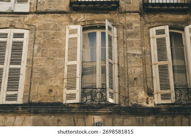Old building facade with open window shutters and textured brick wall, shot on Kodak Portra film in Bordeaux, France